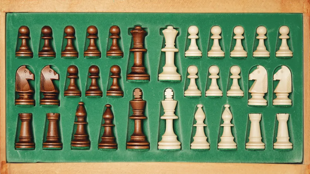 Schachfiguren in einem Kasten mit grünem Inlay, bestehend aus schwarzen und weißen Bauern, Türmen, Läufern, Springern, einer Dame und einem König.
