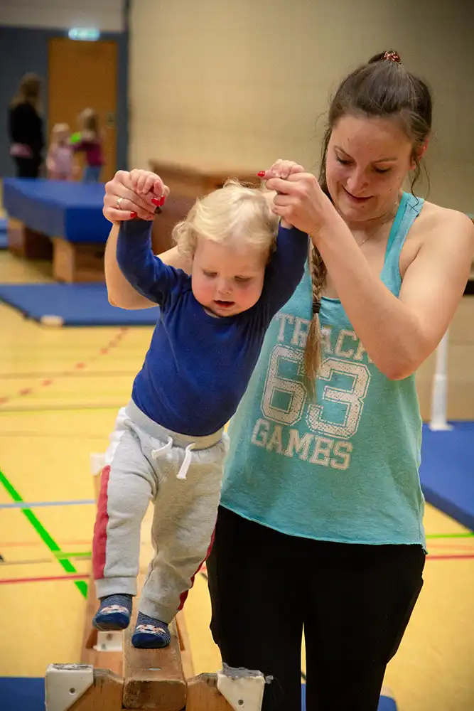 Übungsleiterin Carolin Godderis hilft einem kleinen Kind beim Balancieren auf einem Turngerät im Rahmen des Eltern-Kind-Turnens.