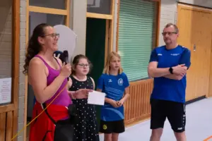 Eine Frau spricht in ein Mikrofon und hält ein Blatt Papier in der Hand, daneben stehen zwei Mädchen und ein Mann. Alle sind versammelt für das Hexennachtturnier 2025 des VfR Simmern.