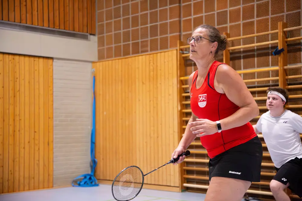 Melanie Wies in einem roten Trikot mit VfR Simmern-Logo spielt im Mixed-Doppel während des Hexennachtturniers 2026. Im Hintergrund ist ihr männlicher Mitspieler in einem weißen T-Shirt zu sehen. Die Halle ist mit Holzverkleidung ausgestattet, und die Atmosphäre ist sportlich und konzentriert.
