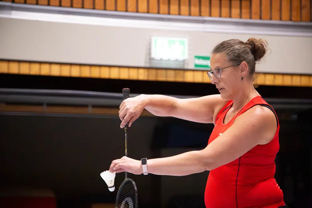 Melanie Wies in einem roten Sportoberteil bereitet sich auf den nächsten Aufschlag vor, während sie einen Federball in der Hand hält. Die Szene zeigt die sportliche Atmosphäre des Hexennachtturniers für Mixed-Doppel, das vom VfR Simmern im Jahr 2026 veranstaltet wird.