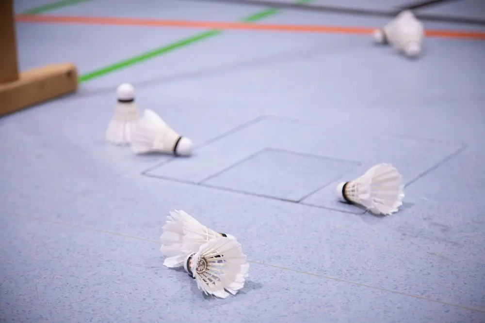 Eine Gruppe von Federbällen liegt auf dem Boden einer Sporthalle, in der sich das 36. Hexennachtturnier 2026 des VfR Simmern abspielt. Die bunten Linien auf dem Boden markieren die Spielfelder, während einige abgenutzte Federbälle verstreut auf dem Boden liegen.