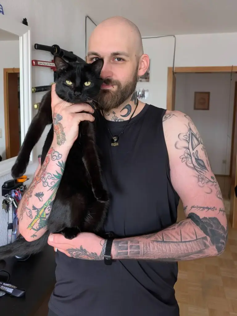 Portrait von Manuel, der eine schwarze Katze auf dem Arm trägt.
