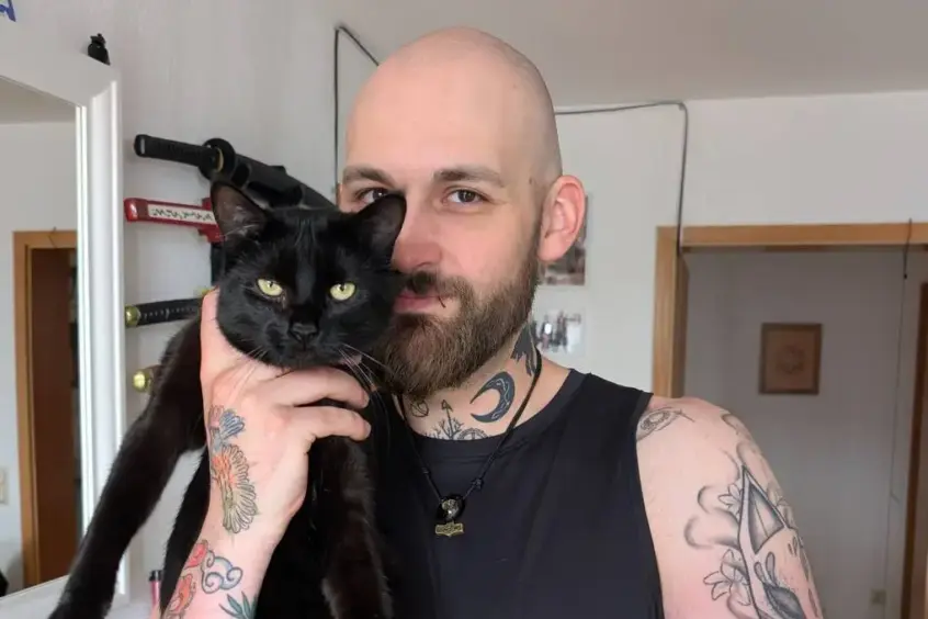 Portrait von Manuel, der eine schwarze Katze auf dem Arm trägt.